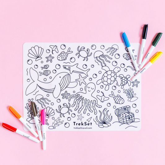 A reusable silicone coloring mat with a under the sea design, accompanied by eight dry erase markers, presented on a pink background.