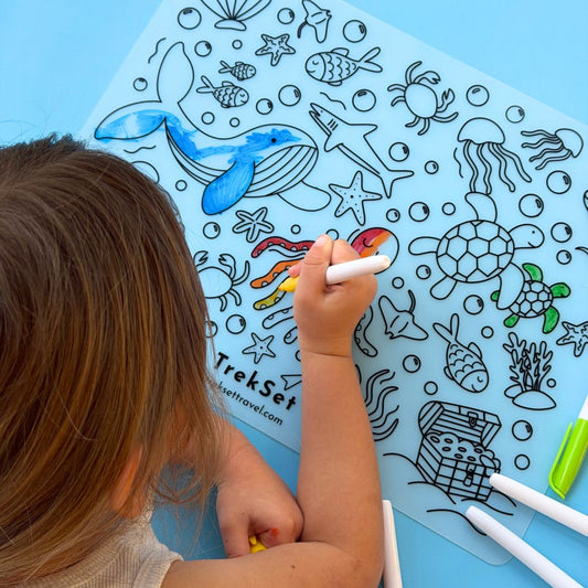 Child coloring an ocean-themed coloring mat with markers on a blue background